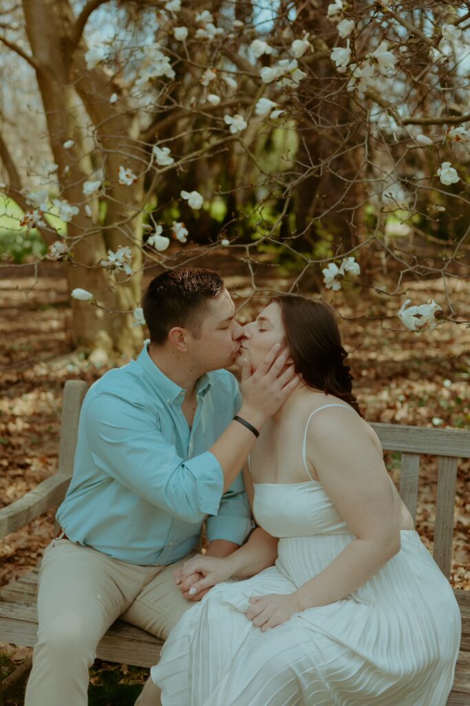 man kissing woman during engagement session on a bench