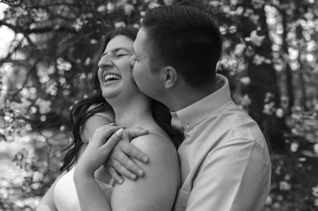 man hugging woman from behind during columbus engagement session and kisses her cheek 