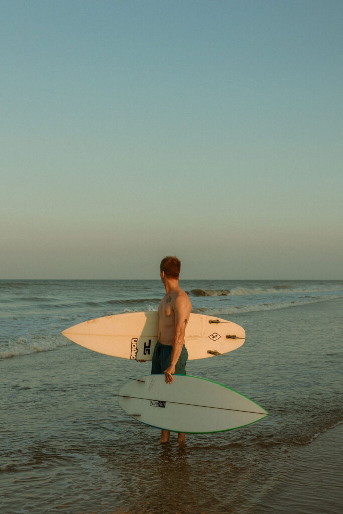 man standing on the beach holding two surf boards