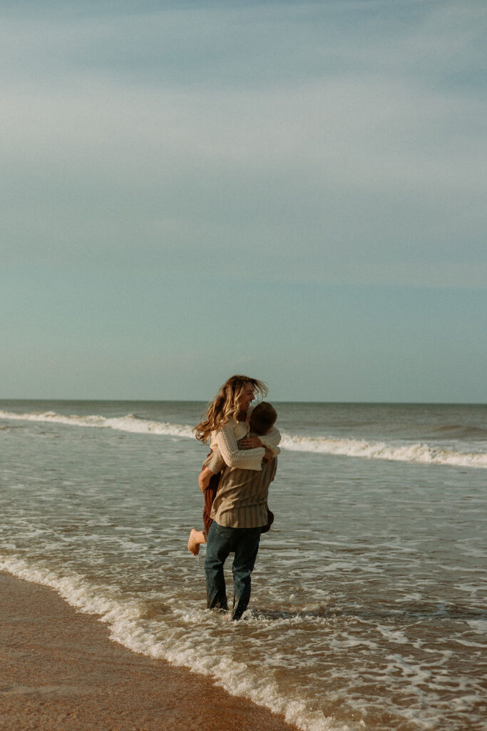 man picking woman up and twirling her around in the ocean