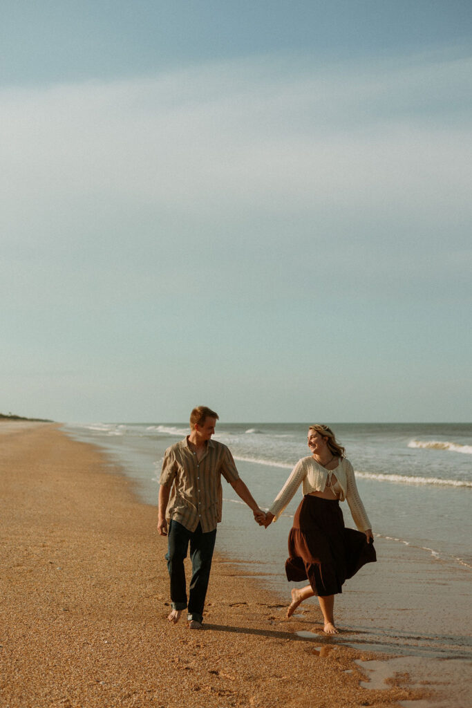 man and woman holding hands while walking on the beach