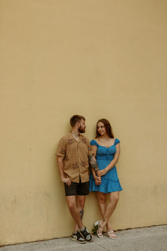 man and woman standing up against a yellow wall