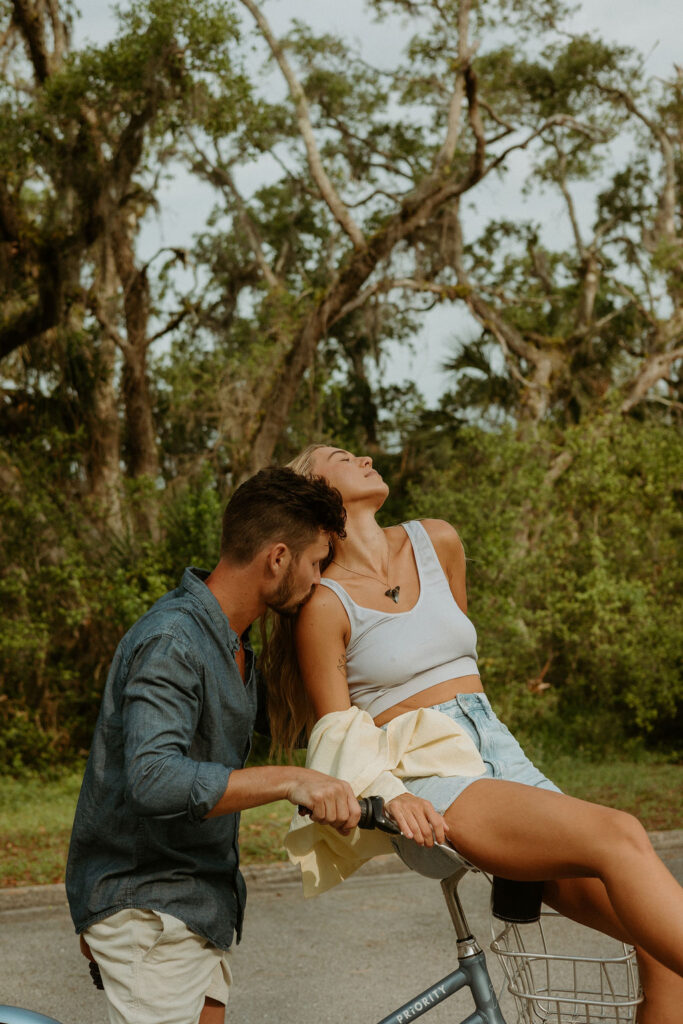 man kissing womans shoulder while sitting on a bike 