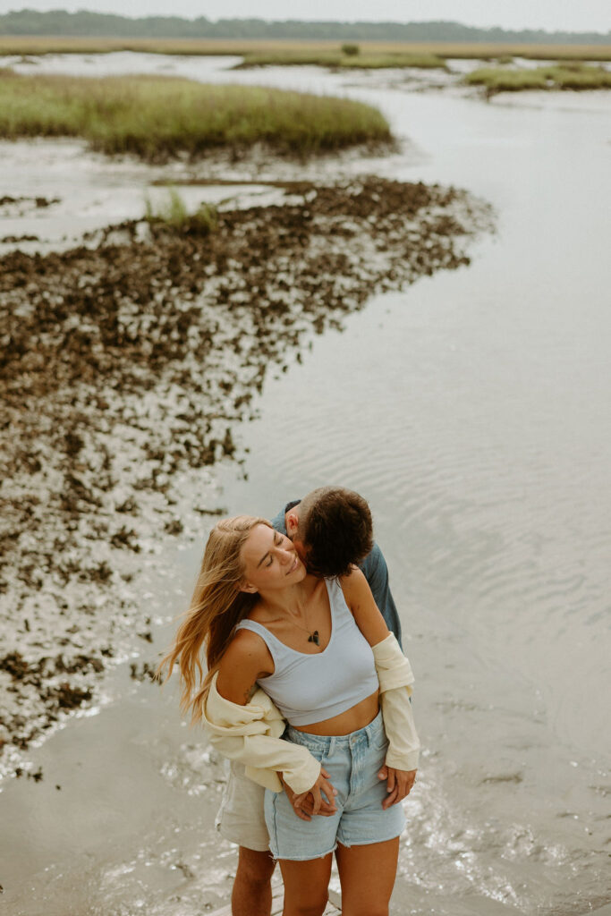 man kissing woman's shoulder by the water 