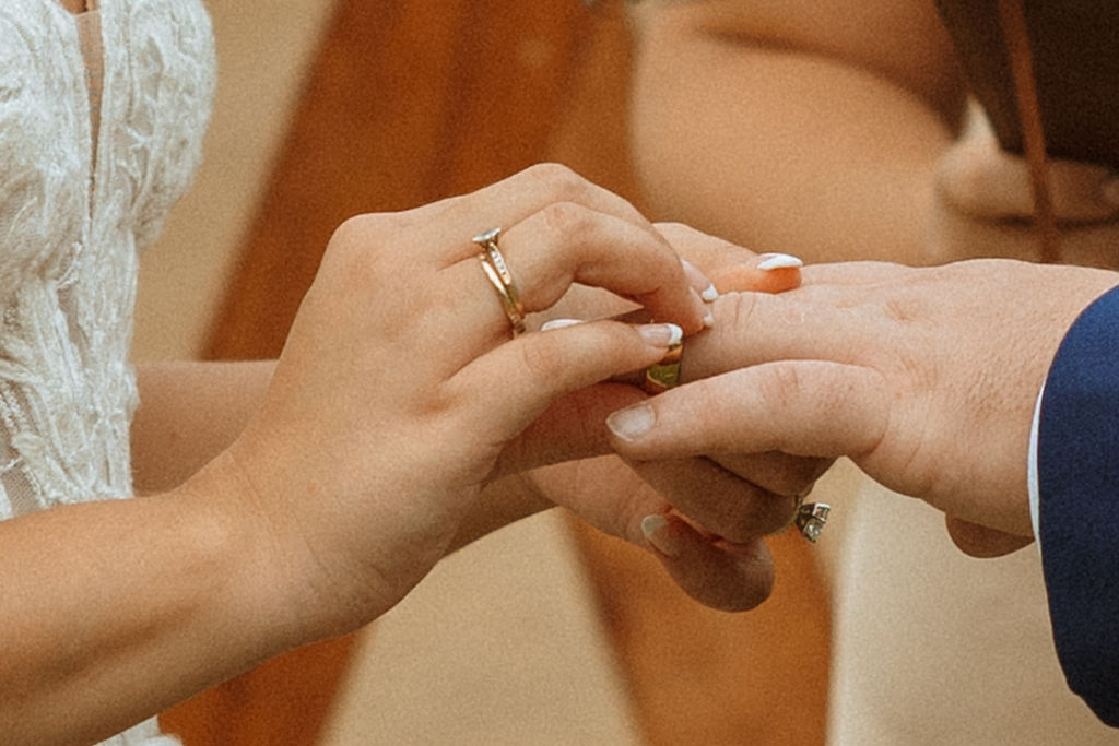 closeup of bride putting grooms wedding band on