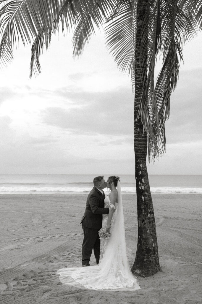 bride and groom kissing under a palm tree