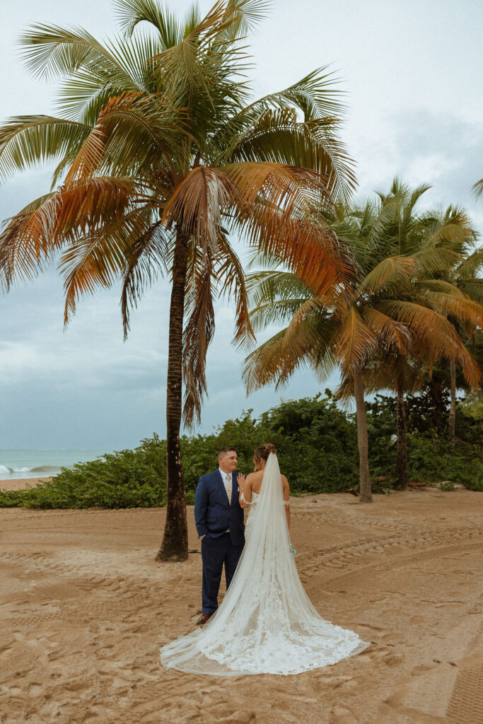 man and woman standing side by side on the beach by palm trees