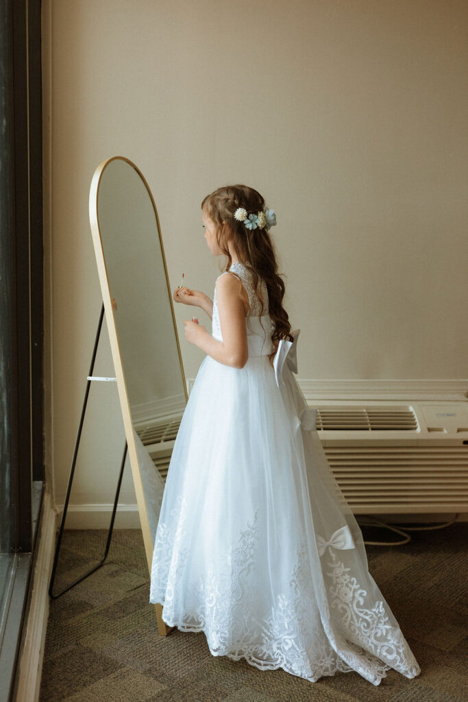 a flower girl applying lipstick in the mirror 