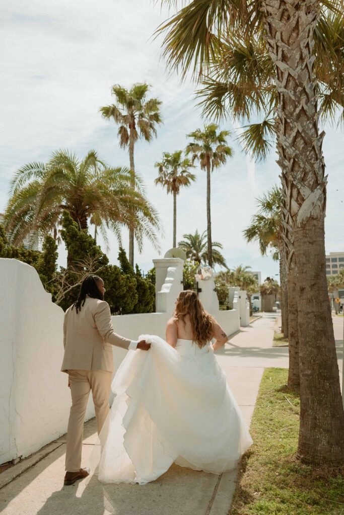 a groom carrying his brides train down the sidewalk on their way to elope