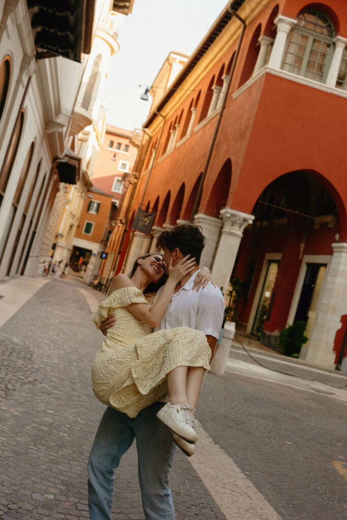 Man carrying girl down the street during their Verona Italy engagement session