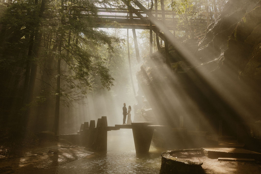 Couple standing on a bridge covered in sun beams during their Hocking Hills elopement