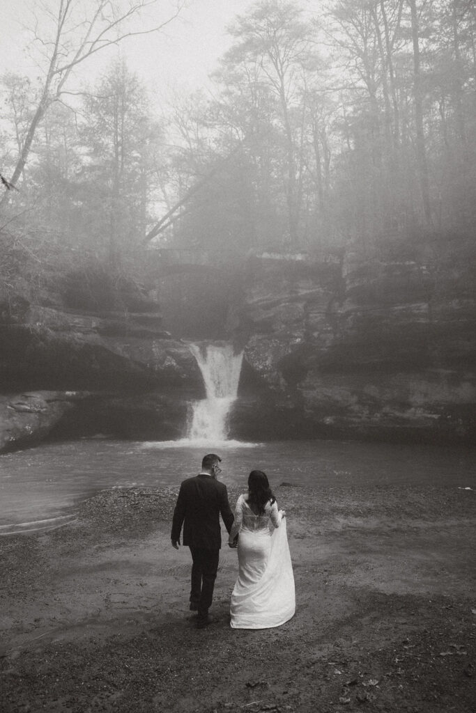 Couple hiking Upper Falls during their moody Hocking Hills elopement
